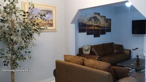 A living room with a brown sofa set, a coffee table, and a potted plant. There is a framed painting on the wall and a flat-screen TV mounted on the wall. - Casa 12-1 - Pet Friendly, Amazing view, and Newly Renovated (San Carlos)
