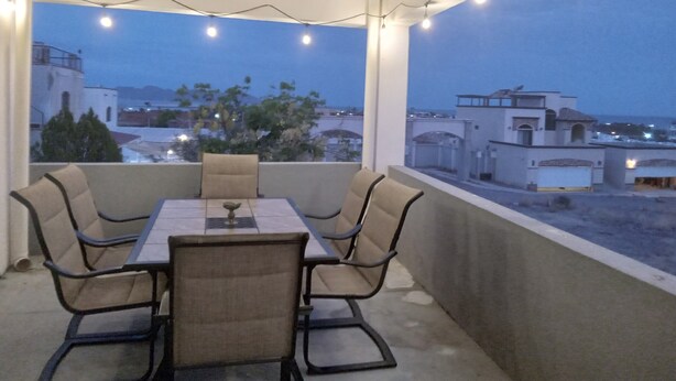 An outdoor balcony with a table and chairs, string lights, and a view of buildings and trees. - Casa 12-1 - Pet Friendly, Amazing view, and Newly Renovated (San Carlos)