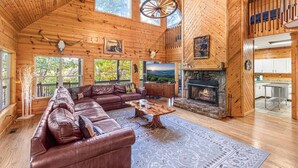 A spacious log cabin interior with a large living area, a stone fireplace, and a dining area.