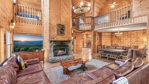 A spacious log cabin interior with a fireplace, leather seating, a dining area, and a balcony.