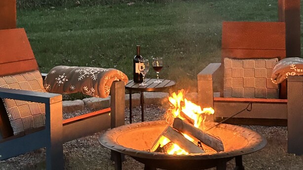 Ein Außenbereich mit Sitzgelegenheit, einem Feuereimer, zwei Stühlen und einem Tisch mit einer Flasche und einem Glas.