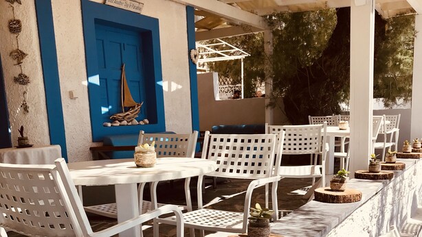 A covered outdoor seating area with white chairs and tables, a blue door, and decorative plants.