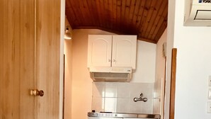A compact kitchen with white cabinets, a stainless steel refrigerator, and a wooden ceiling.