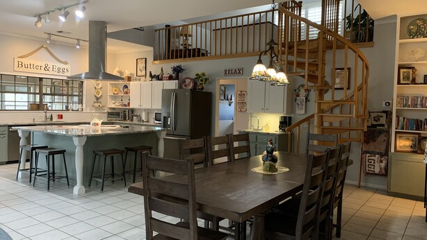 A spacious kitchen with a central island, a dining area with wooden chairs, and a spiral staircase leading to an upper level. - Country Home on 33 acres,  sleeps 18, On the San Saba River! (Voca)