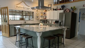 A modern kitchen with a central island, bar stools, a refrigerator, and a sign reading "Butter & Eggs". - Country Home on 33 acres,  sleeps 18, On the San Saba River! (Voca)