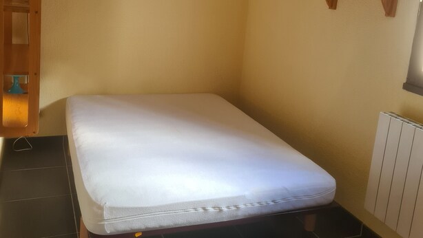 A small, single-bed room with a wooden headboard, a bedside table with a lamp, a small shelf, and a radiator. - Apartment at the foot of the slopes - STATION LE PLEYNET (Le Pleynet)