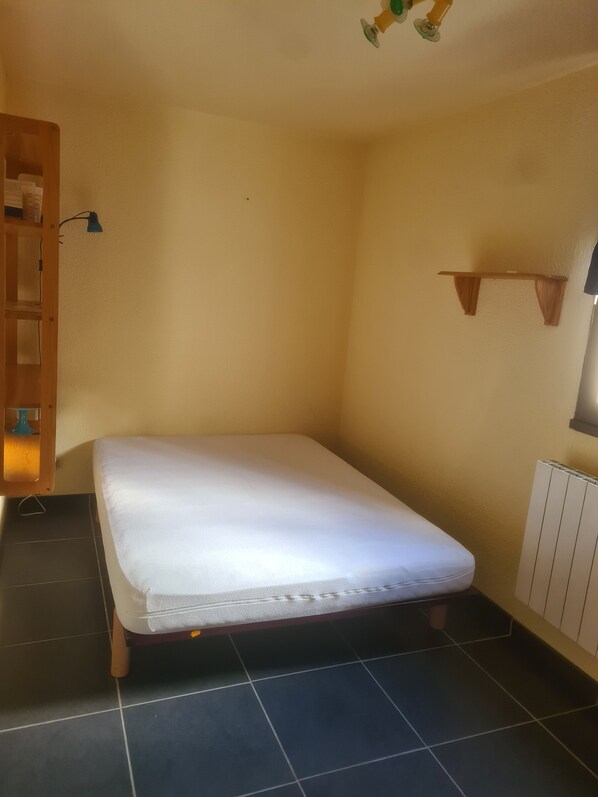A small, single-bed room with a wooden headboard, a bedside table with a lamp, a small shelf, and a radiator. - Apartment at the foot of the slopes - STATION LE PLEYNET (Le Pleynet)