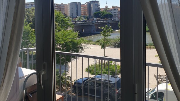 Vista desde un balcón con barandilla metálica, sobre un estacionamiento con coches y un río.