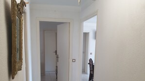Un pasillo con una mesa y sillas, un candelabro, y una puerta que da a otra habitación.