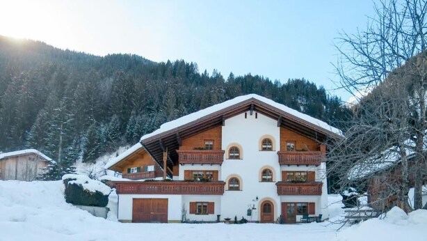 Un chalet de varios pisos con techo inclinado, balcones de madera y un paisaje cubierto de nieve.