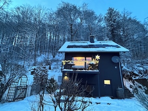 Uma cabana com varanda, rodeada por árvores cobertas de neve.