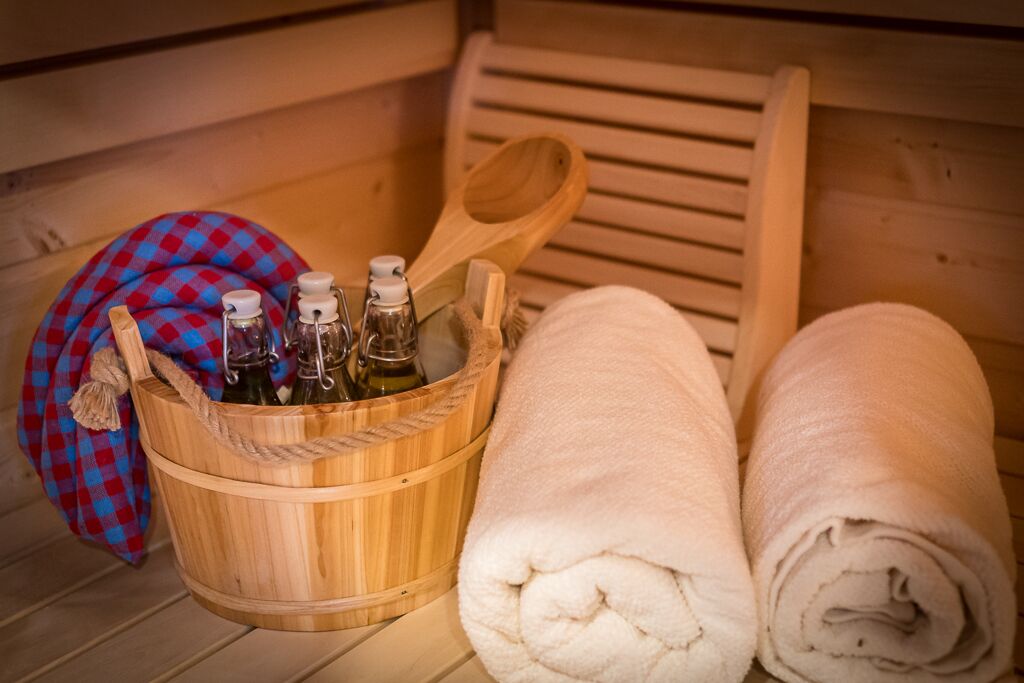 A wooden tub with bottles, a wooden spoon, and rolled towels.