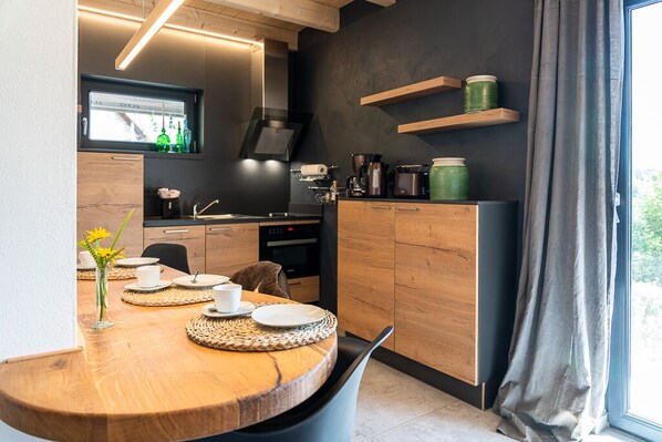 A modern kitchen with wooden cabinets, a built-in oven, and a dining area with a round table and chairs.