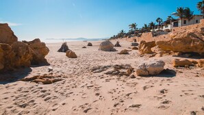 A desert beach with large rocks, palm trees, and a clear sky. - 3 BD Oceanview Penthouse with infinity pool and jacuzzi (San Jose del Cabo)