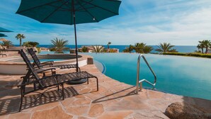 A pool area with lounge chairs and an umbrella, surrounded by stone tiles and palm trees, overlooking a clear blue sky. - 3 BD Oceanview Penthouse with infinity pool and jacuzzi (San Jose del Cabo)