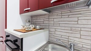 Una cocina con salpicadero de piedra, un lavamanos de acero inoxidable y armarios rojos.