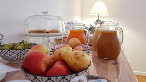 Una mesa de desayuno con diversas frutas, una jarra de jugo de naranja y un vaso de té helado.