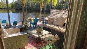 Un patio con mobiliario de mimbre, una mesa con objetos decorativos y vistas a una masa de agua tranquila.