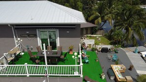 Relax on the spacious deck with a dining table, sofa, and lounge chairs, surrounded by lush tropical surroundings and a serene body of water.