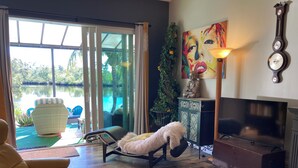 Una sala de estar con sofá, un perro, televisor y vista a una piscina.