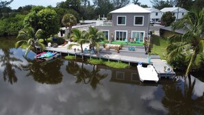 Una casa con un muelle que se adentra en el agua, rodeada de vegetación y palmeras.