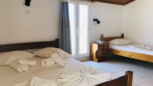 Een hotelkamer met een groot bed, een kleiner bed, een nachtkastje met een telefoon en een raam met gordijnen.