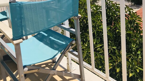 Een balkon met uitzicht op zee, een stoel en een tafel.
