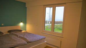 Une chambre avec deux lits, une fenêtre donnant sur l’extérieur et un luminaire fixé au mur.
