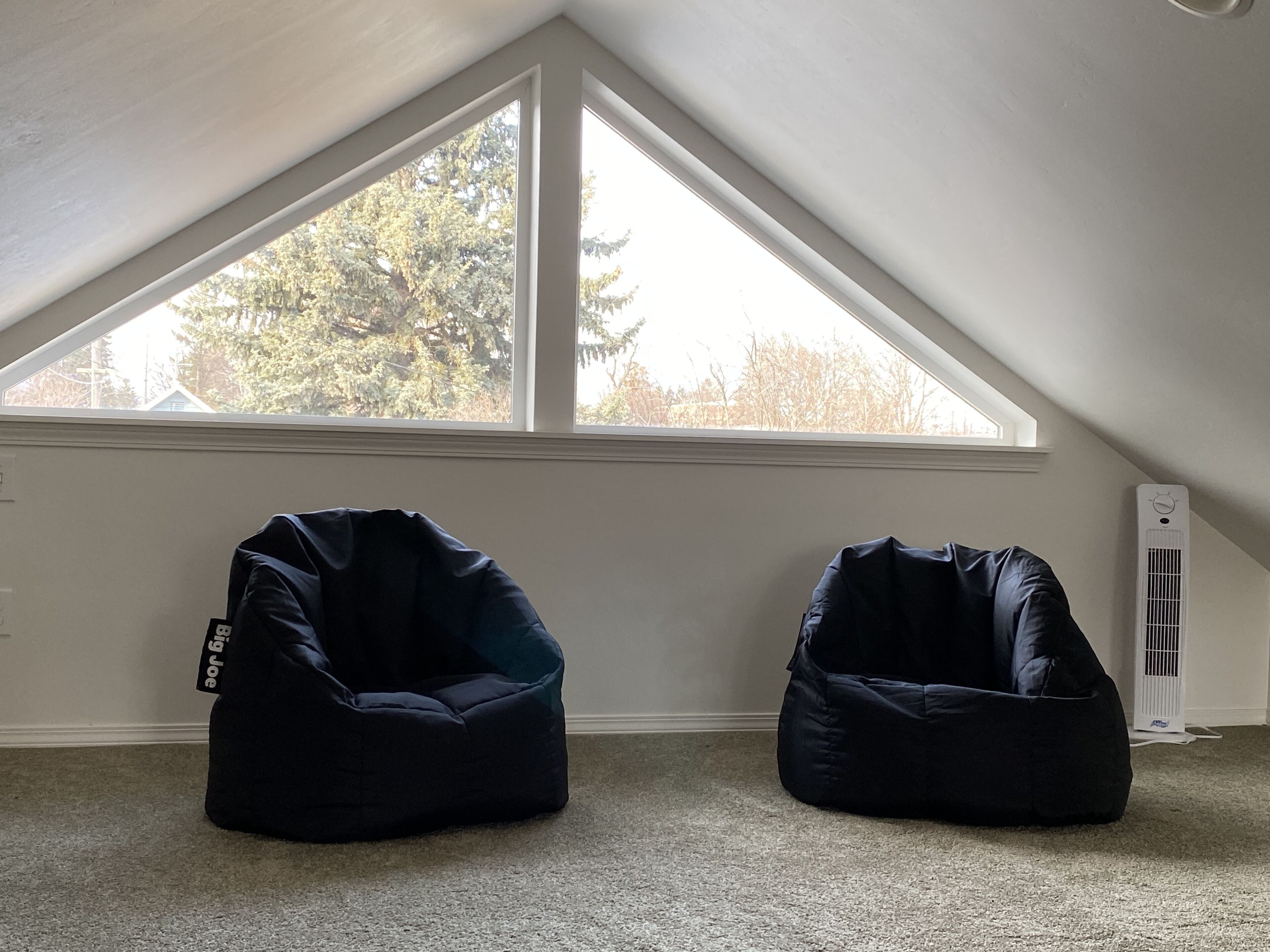 A room with a sloped ceiling and a large window. There are two bean bag chairs and a white radiator.