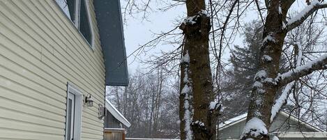 Un quartier résidentiel enneigé avec une maison, une clôture en bois et un arbre.