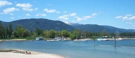 A lakeside view with boats, a sandy beach, and mountains in the background.