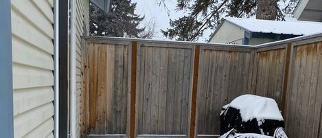 A snow-covered backyard with a wooden fence, a patio table, and a chair.