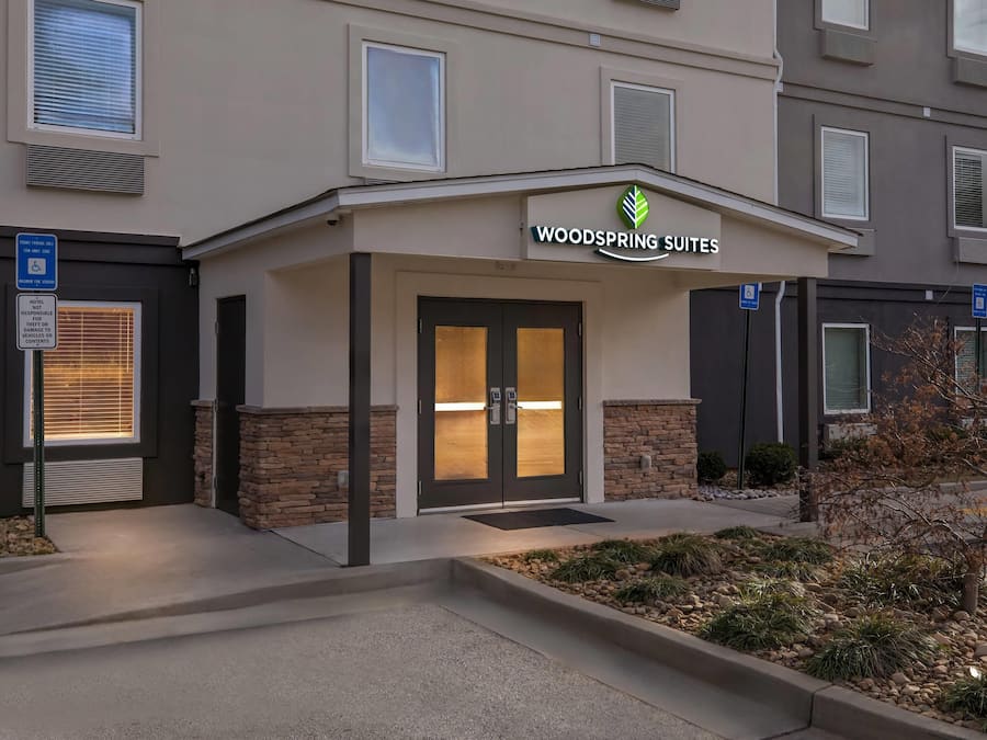 A hotel entrance with a sign for 'Woodspring Suites' and a wheelchair-accessible entrance.