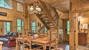 A wooden cabin interior with a dining table, chairs, a staircase, a sofa, and a kitchen area. - Peaceful Cabin on 3 Private Acres: Deck & Fire Pit (Blairsville)