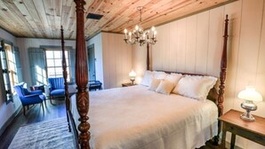 Un grand lit à baldaquin agrémenté d’un lustre, avec un plafond en bois et une vue sur l’extérieur par une fenêtre.