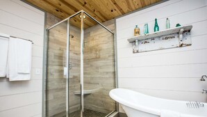 Une salle de bain moderne avec une douche à parois de verre, une baignoire sur pieds et une étagère ornée de bouteilles anciennes.