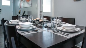 Una mesa de comedor dispuesta con platos, tazones, vasos y cubiertos blancos, de diseño moderno y con vista al salón.