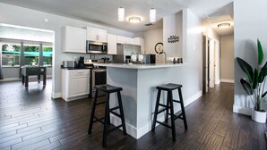 Cocina moderna con armarios blancos, electrodomésticos de acero inoxidable, una isla central con taburetes e iluminación colgante.