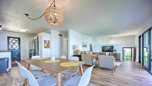 Una cucina moderna con mobili bianchi, un'area pranzo con tavolo e sedie di legno, e un soggiorno con divano e televisore.