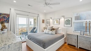 Ein Schlafzimmer mit Bett, Schreibtisch, Stuhl, einem Balkon mit Aussicht und Kunstwerken an den Wänden.