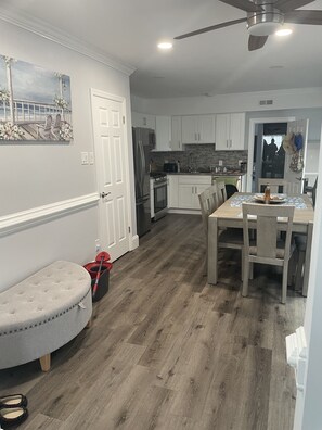 A kitchen with white cabinets, a dining table, and a ceiling fan. - Beach Summer House (Ventnor)