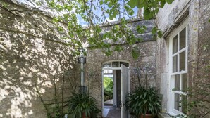 Un edificio de piedra con un acceso que da a un jardín. Hay plantas en macetas a ambos lados de la entrada.