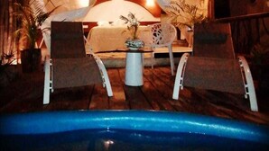 Uma área de estar acolhedora ao ar livre, com um telhado de palha, piscina e plantas em vasos.