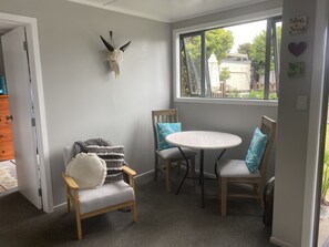 Une pièce chaleureuse avec une table ronde, deux chaises, un fauteuil en bois agrémenté d’un coussin, et un crâne de cerf accroché au mur.