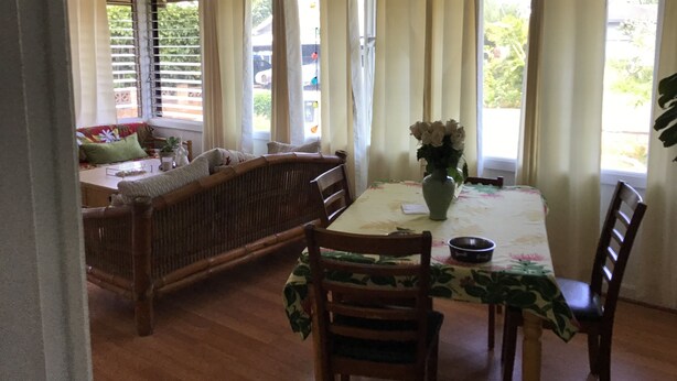 Un comedor con una mesa, sillas, un ventilador de techo y una ventana con cortinas.