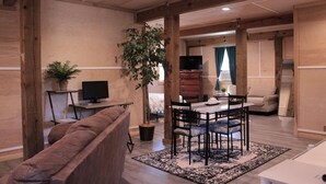 A cozy living room with a brown sofa, a dining table with chairs, a TV, and a potted plant. - The best OBX sunsets (Waves)