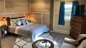 A bedroom with a bed, bedside lamps, a dresser, a television, and a view of the outdoors. - The best OBX sunsets (Waves)