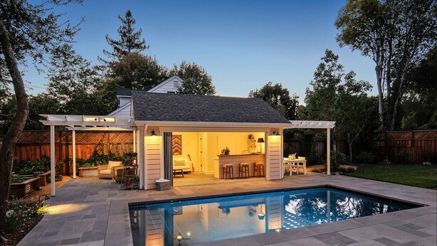 Un patio trasero con piscina, terraza techada y un pequeño bar.