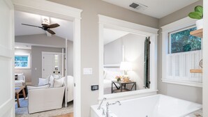 Un baño moderno con una bañera blanca grande, un ventilador de techo y una ventana con persianas.