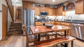 Una cocina moderna con armarios de madera, electrodomésticos de acero inoxidable y un comedor con mesa y banco.